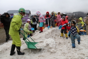 雪山を作る作業員と雪遊びをしながらその様子をみている園児たち