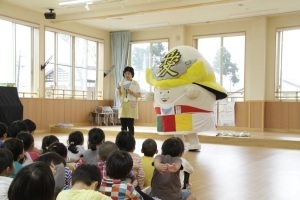 園児たちに米の大切さを説明する栄養士とこめつぐ君