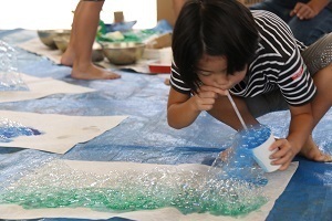 液体の絵の具にストローで息を吹きかけて泡を出し、その泡を和紙に垂らして色や模様をつけている様子
