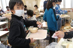 梅干しやごはんなどの配膳の順番を待つ児童