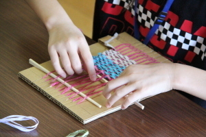 段ボールの機織りでコースターを作っている様子