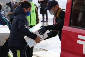 郵便局員に雪の入った容器を渡す様子