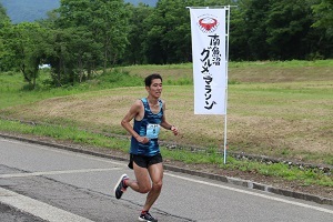 国際大学前にあるグルメマラソンの旗の近くを走るランナー