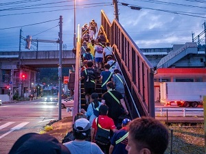 浦佐駅踏切付近の連絡橋の階段を上る参加者