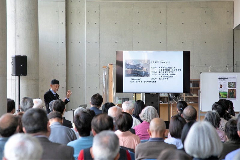 大村智 博士が大勢の参加者の前で講演する様子